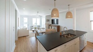 A modern kitchen with a black countertop, white cabinetry, and a dining area with a wooden table and chairs. - Allure by Mira-Mar (Wrightsville Beach)