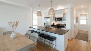 A modern kitchen with white cabinets, stainless steel appliances, and a central island with bar stools. - Allure by Mira-Mar (Wrightsville Beach)