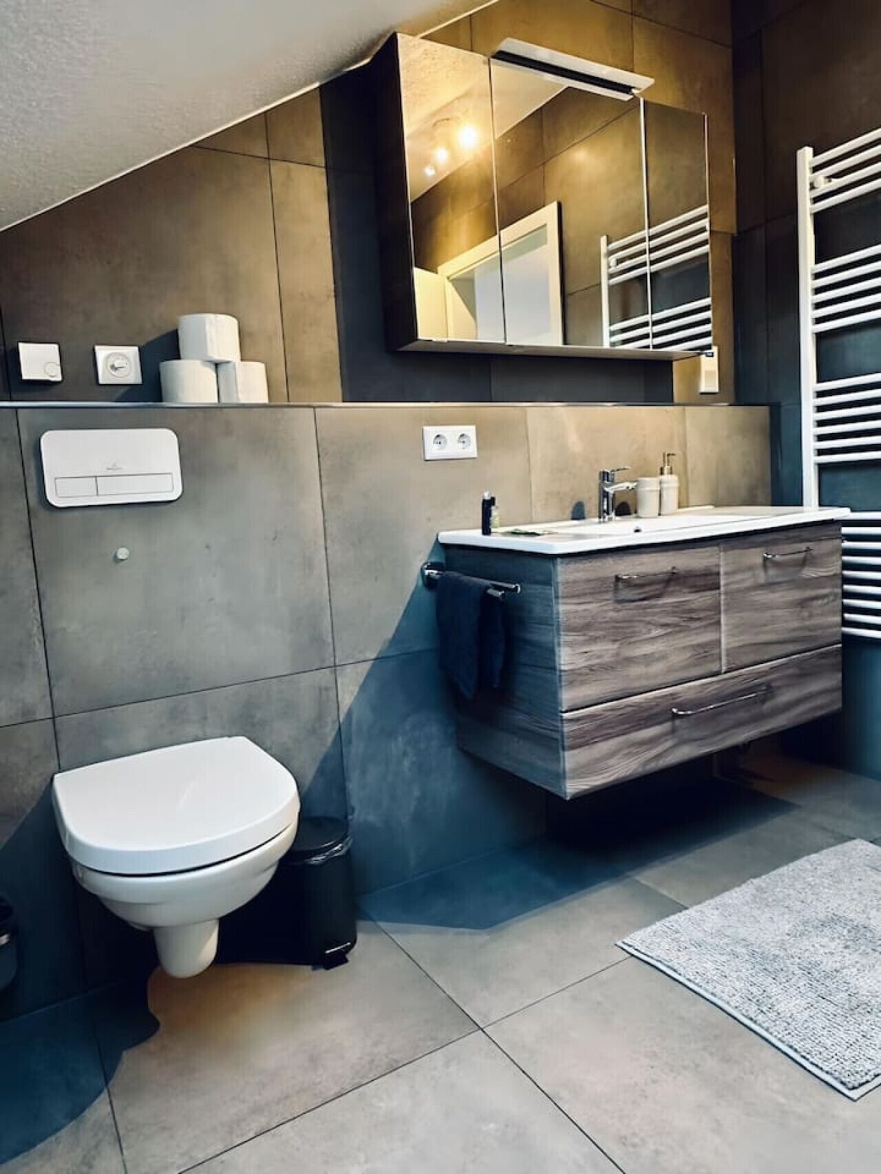 Et moderne badeværelse med toilet, vaskebord og et stort spejl.