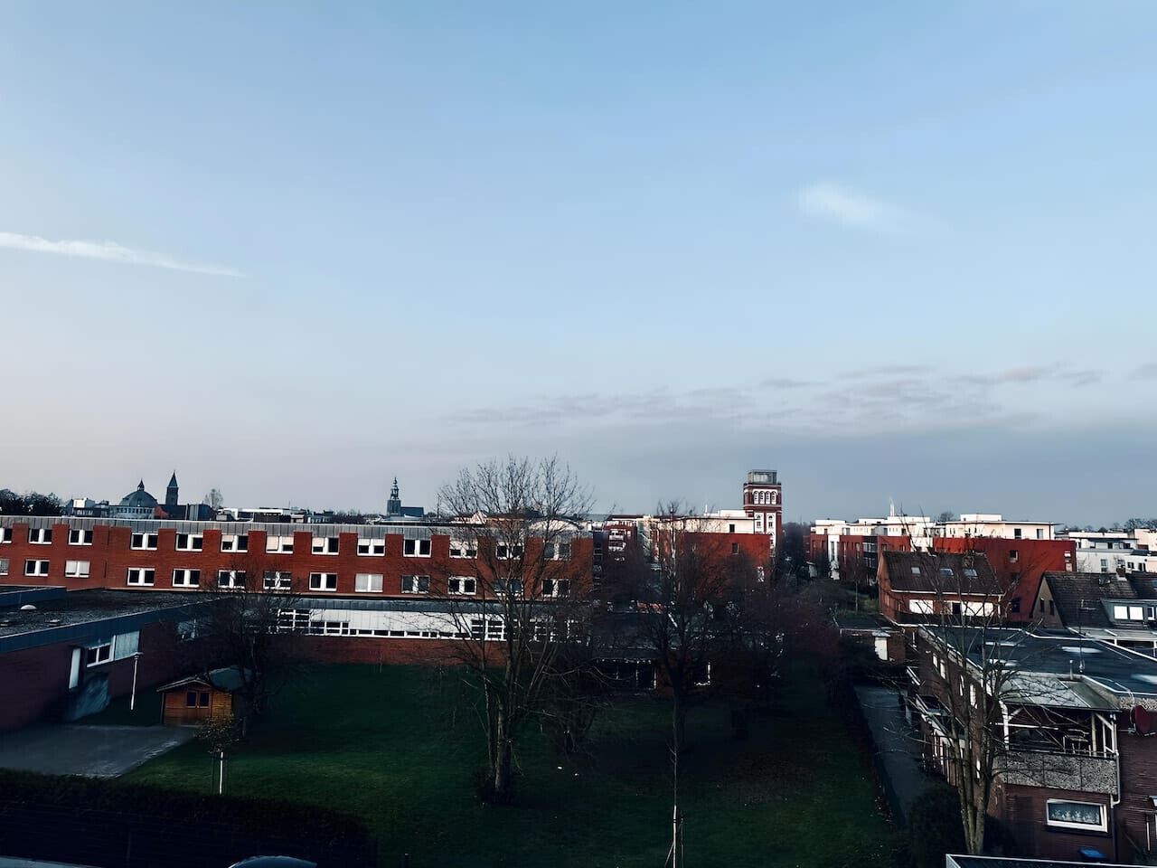 Un edificio de varios pisos con fachada de ladrillo rojo, múltiples ventanas y una pequeña estructura similar a una torre.