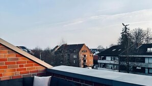 Eine Dachterrasse mit einem Holztisch, einer dunkelgrauen Couch und einer Backsteinwand.