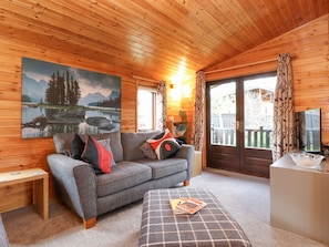 Een knus houten interieur met een houten plafond, een grijze bank met kussens, een kleine tafel en een schilderij van een meer.