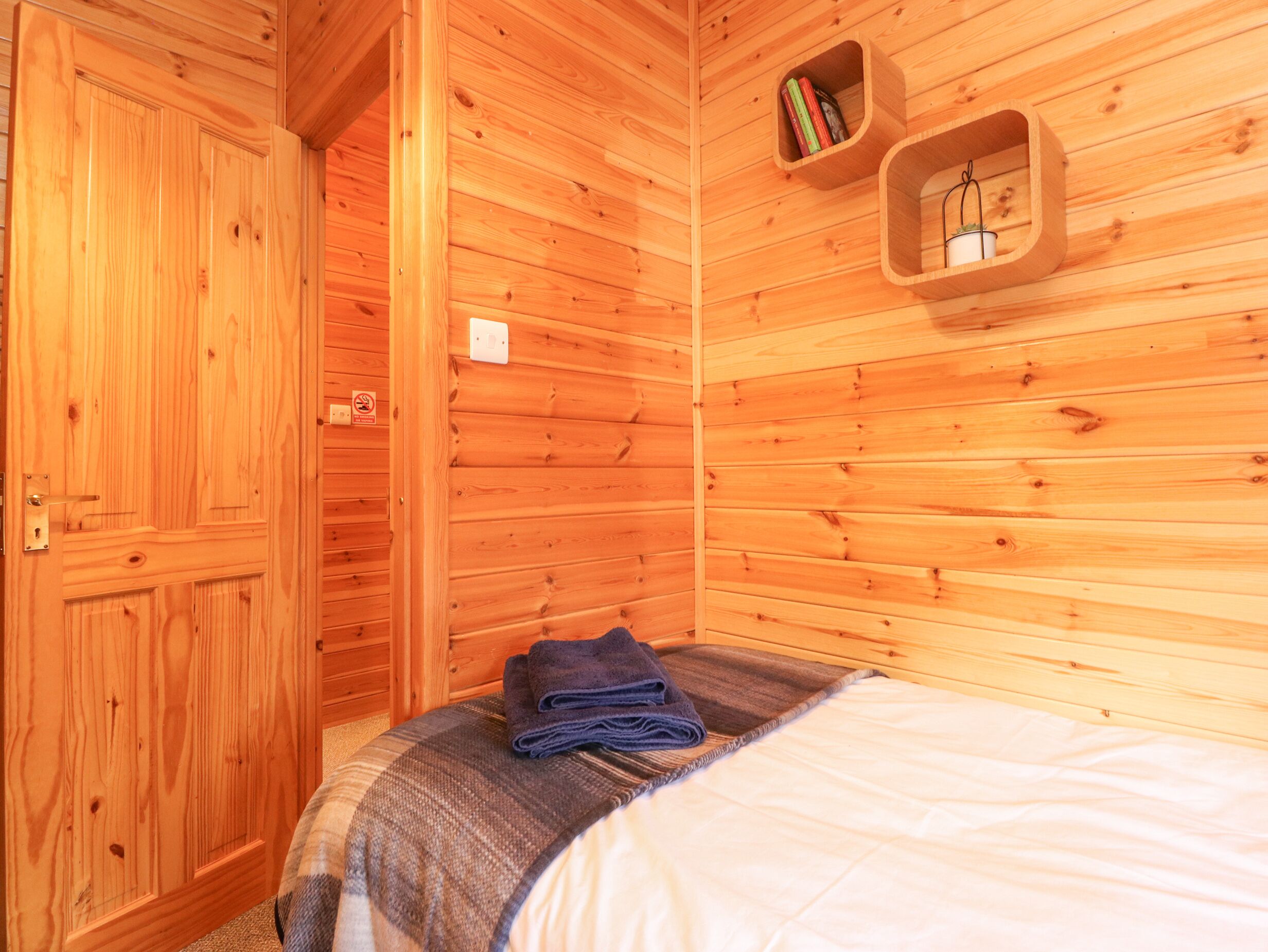 Une pièce en bois avec un lit, une porte et une étagère contenant des livres et une plante.