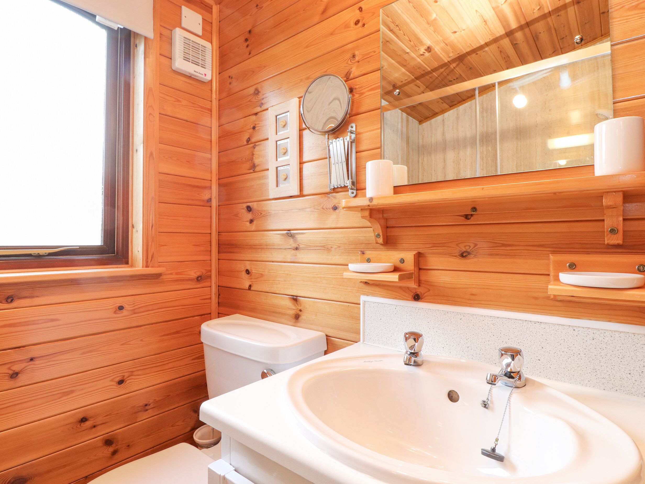 Une salle de bain rustique, aménagée dans une cabane en bois, avec des toilettes, un lavabo et un miroir.