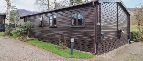 A single-story wooden cabin with a number 19 sign, a gravel driveway, and a small garden area.