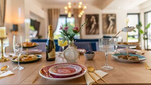A dining table set with plates, glasses, and a bottle, surrounded by chairs and a vase with flowers. - Villa Lux ZadarVillas (Zemunik)