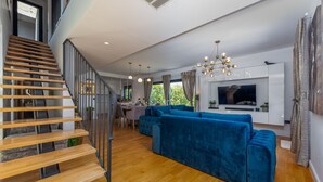 A modern living room with a wooden staircase, a blue sofa set, and a dining area. - Villa Lux ZadarVillas (Zemunik)