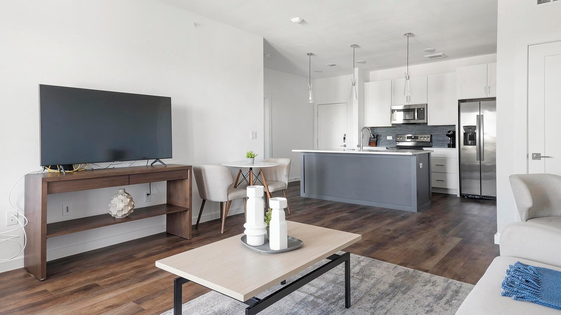 Een moderne woonkamer met een flatscreen televisie, een houten console tafel, een salontafel en een zithoek met twee fauteuils.