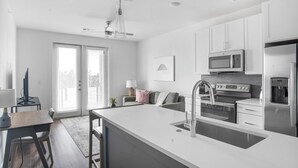 A modern kitchen with a central island, stainless steel appliances, and a dining area with a table and chairs. - Landing | Beautiful 1BD, Clubhouse, Pool (Bee Cave)