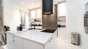 Una cocina moderna con armarios blancos, una isla central, una campana extractora negra y un cubo de basura de acero inoxidable.