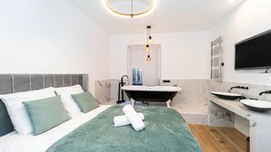 Un dormitorio moderno con una cama grande, una manta verde y una toalla blanca bien doblada.