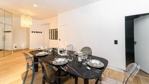 Comedor con una mesa de mármol negro dispuesta para seis personas, sillas transparentes y una araña.