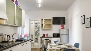 A compact kitchen with a microwave, refrigerator, and a dining area with a table set for two. - Art and Comfort Near Lomellini Street by Wonderful Italy (Genoa)