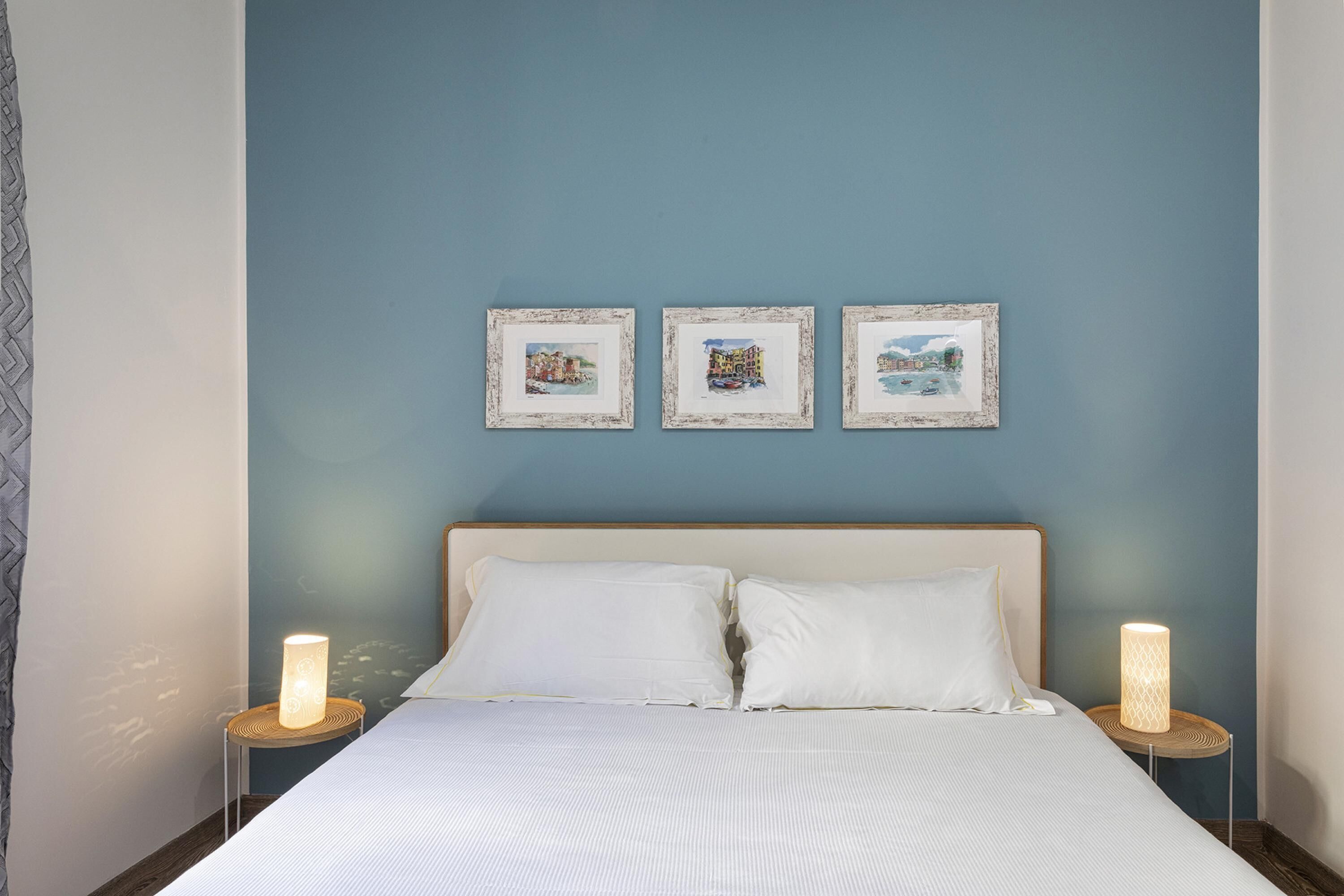 A neatly made bed with white linens, two bedside lamps, and three framed pictures on the wall.