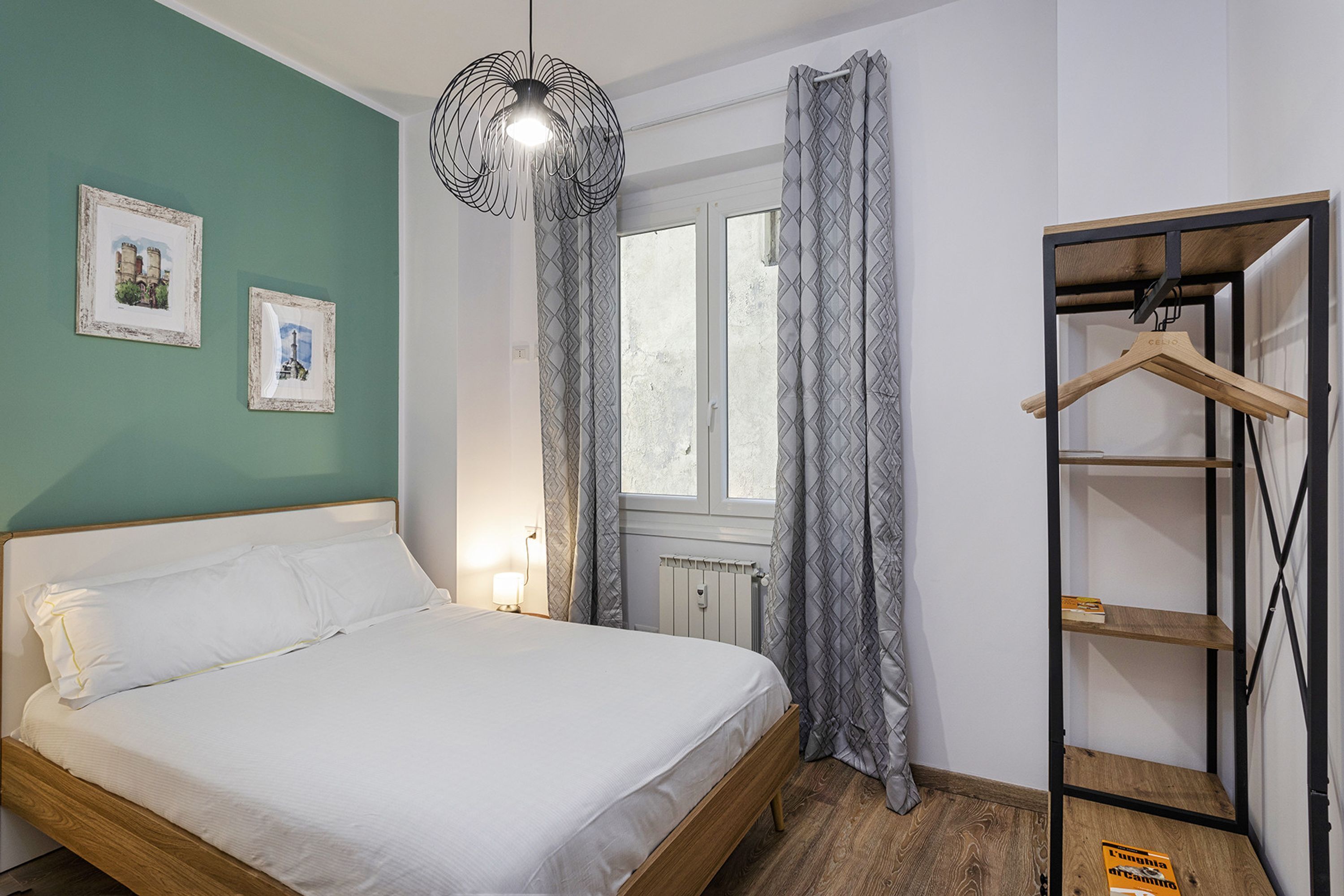 Un lit bien fait dans une pièce dotée d’une fenêtre, d’un radiateur et d’un porte-manteau en bois.