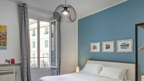 A bedroom with a bed, a window with curtains, a wall-mounted light fixture, and framed pictures. - Art and Comfort Near Lomellini Street by Wonderful Italy (Genoa)