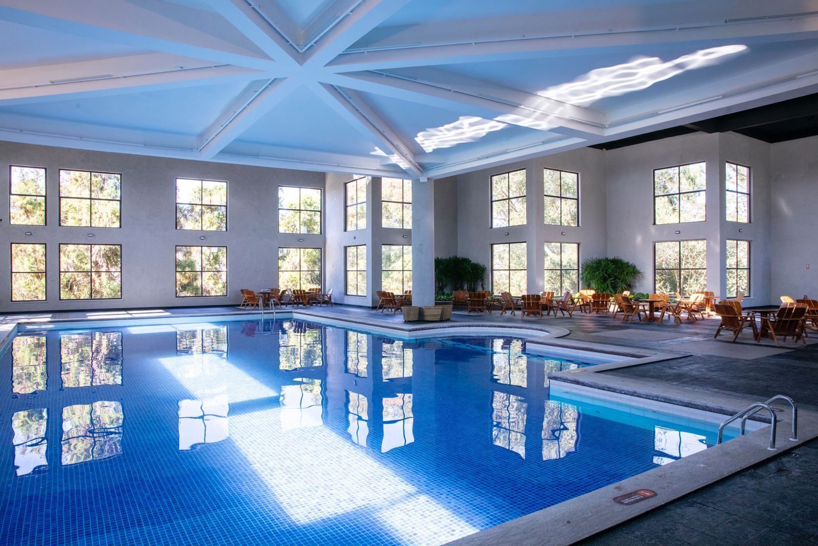 A large indoor swimming pool with clear reflections, surrounded by large windows and outdoor views.
