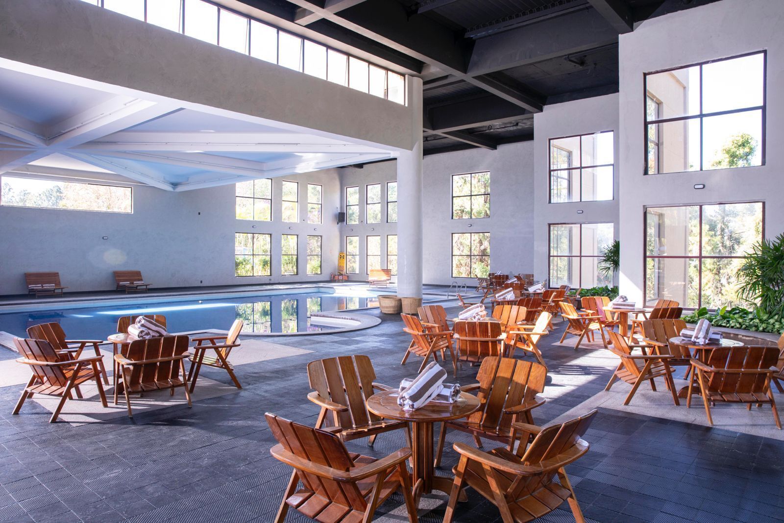 Amplia zona de piscina interior con diversas opciones de descanso y grandes ventanales que dejan entrar luz natural.