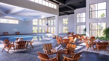 Amplia zona de piscina interior con diversas opciones de descanso y grandes ventanales que dejan entrar luz natural.