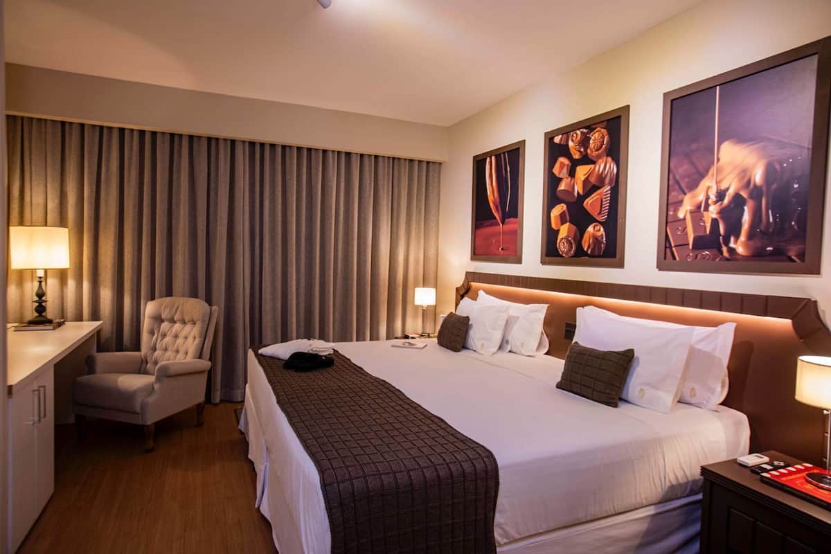 A hotel room with a large bed, a desk, a chair, and a nightstand.