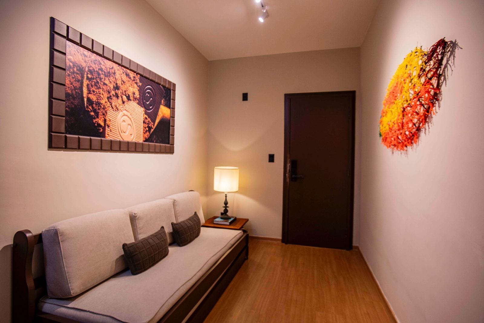 A modern room with a sofa, a wall-mounted artwork, a lamp, and a door.