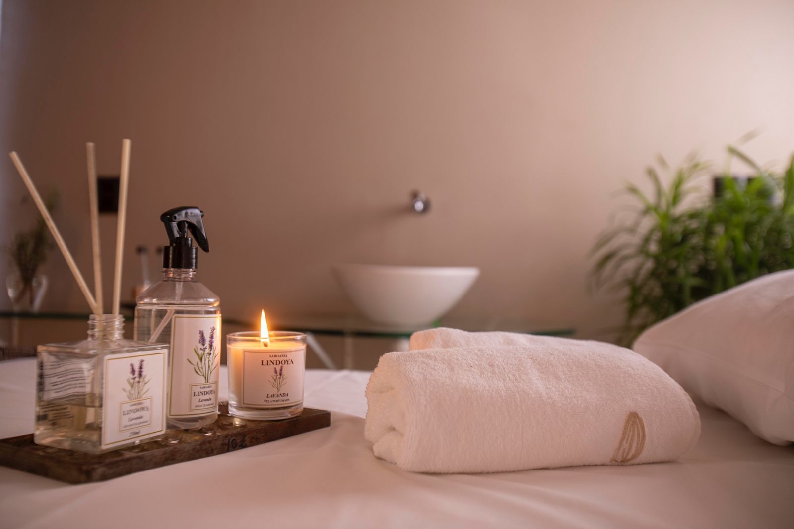 A neatly arranged bathroom with a white sink, a lit candle, and two bottles of Lindoya lavender-scented products on a tray.