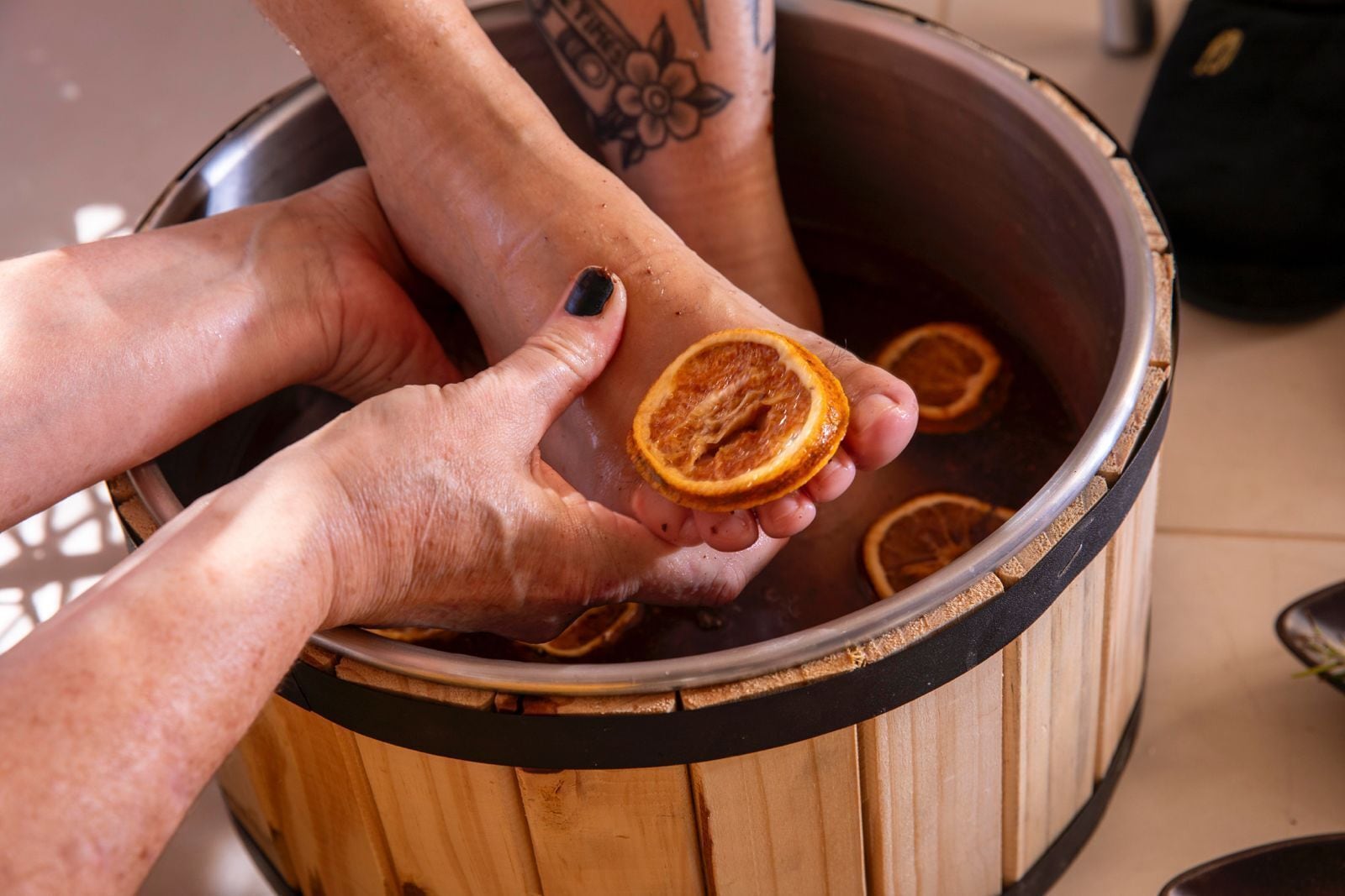 A person soaking their feet in a wooden tub with dried orange slices.