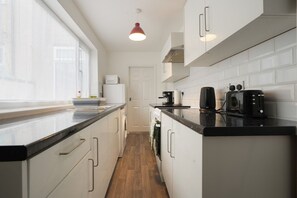 Et moderne køkken med hvide skabe, en sort bordplade og en rød hængende lampe.