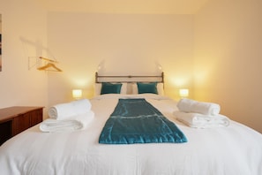 Una habitación de hotel con una cama bien hecha, dos lámparas de noche y una mesita de noche de madera.
