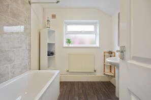 Ein modernes Badezimmer mit Badewanne, Fenster, Heizkörper und Waschbecken.