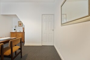 A room with a white door, a wooden cabinet, a dining table with chairs, and a large mirror on the wall. - Peaceful Grimsby House w/ Fast WiFi & Garden (Grimsby)