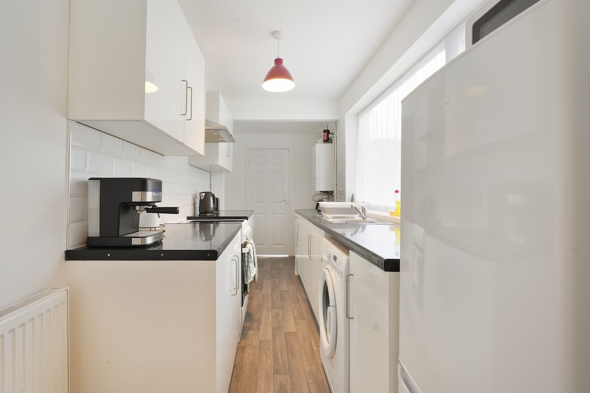 Een moderne keuken met witte kasten, een koffiezetapparaat, een wasmachine en een koelkast.