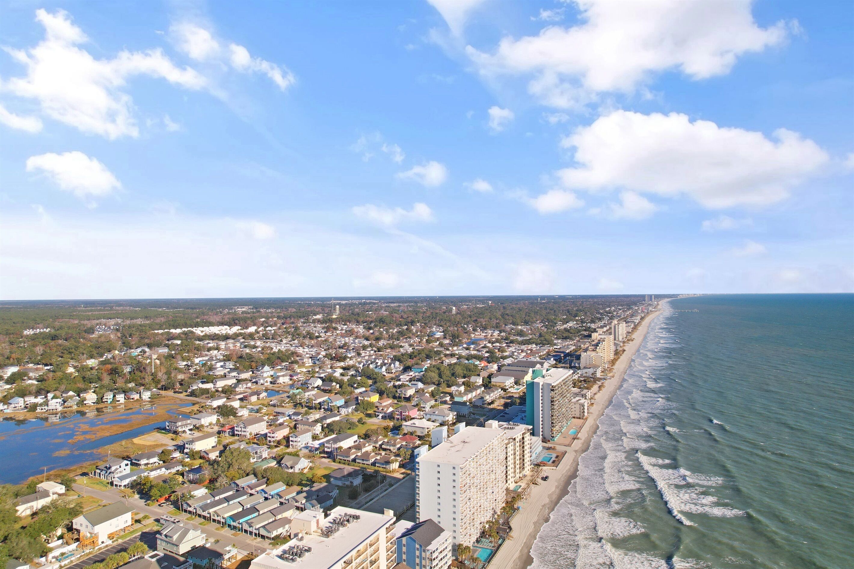 Vista aérea de un pueblo costero con playa, edificios residenciales y un gran hotel.