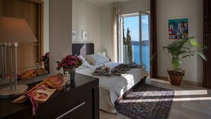 Una camera da letto con un letto, una cassettiera, una lampada, una pianta e vista sul mare.
