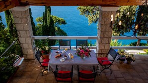 Una terrazza con tovaglia a scacchi, cuscini rossi e vista mare.