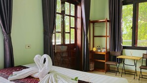 A hotel room with a bed, a desk, and a chair. There is a window with curtains, and a door leading outside. - Vi TamCoc Hotel (Nam Hoa Lu)