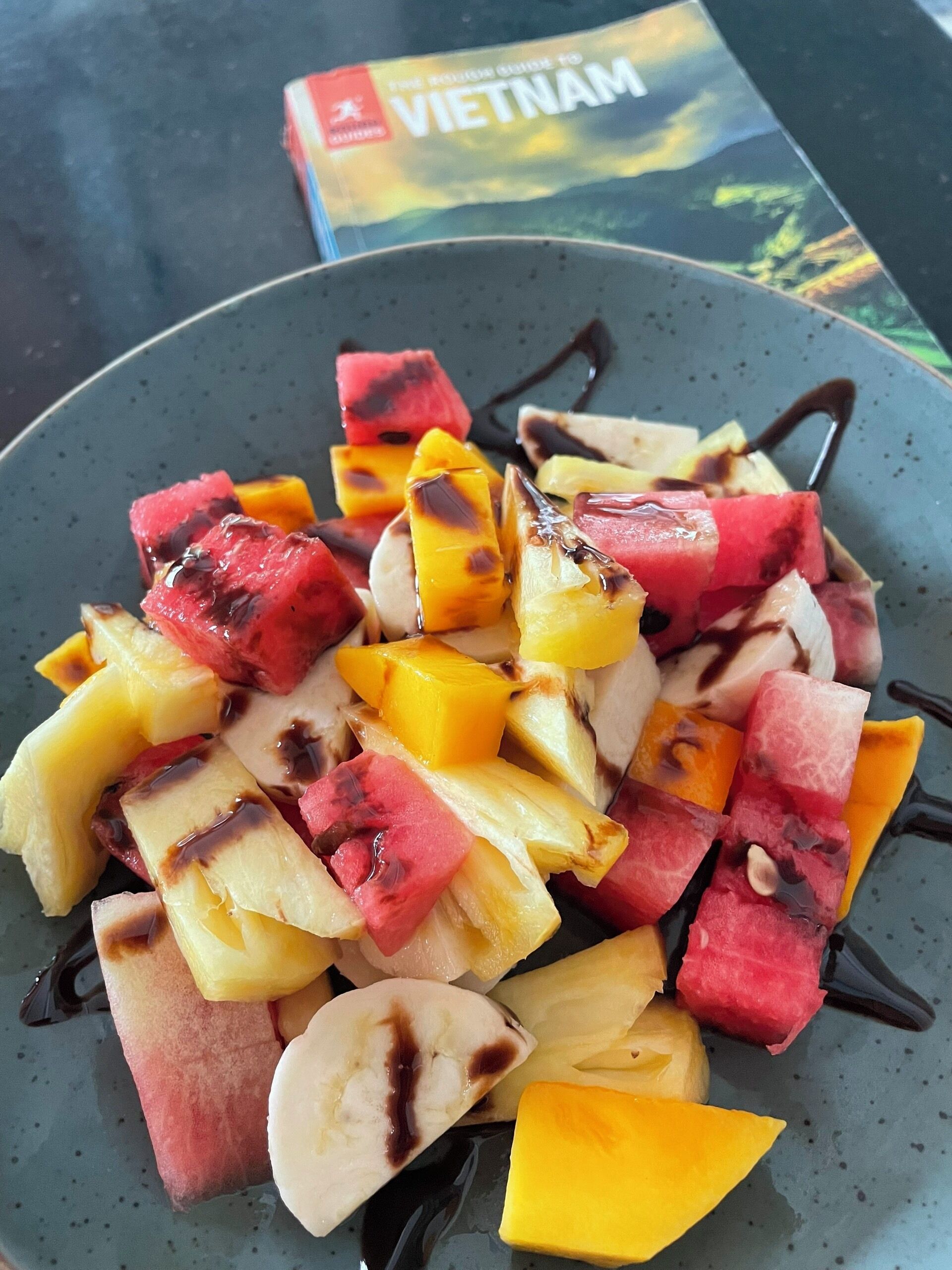A plate of fruit salad with various fruits and chocolate sauce.