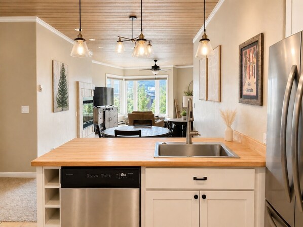 A modern kitchen with a dishwasher, a sink, and a refrigerator. There is a dining area with a round table and chairs, and a ceiling fan. - Remodeled Eolus Ski in/Ski Out condo - Slope & Mountain Views - Deck (Durango)