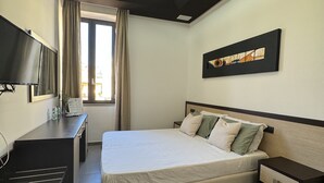 Una habitación de hotel moderna con cama, mesitas de noche, escritorio, televisor y ventana con cortinas.