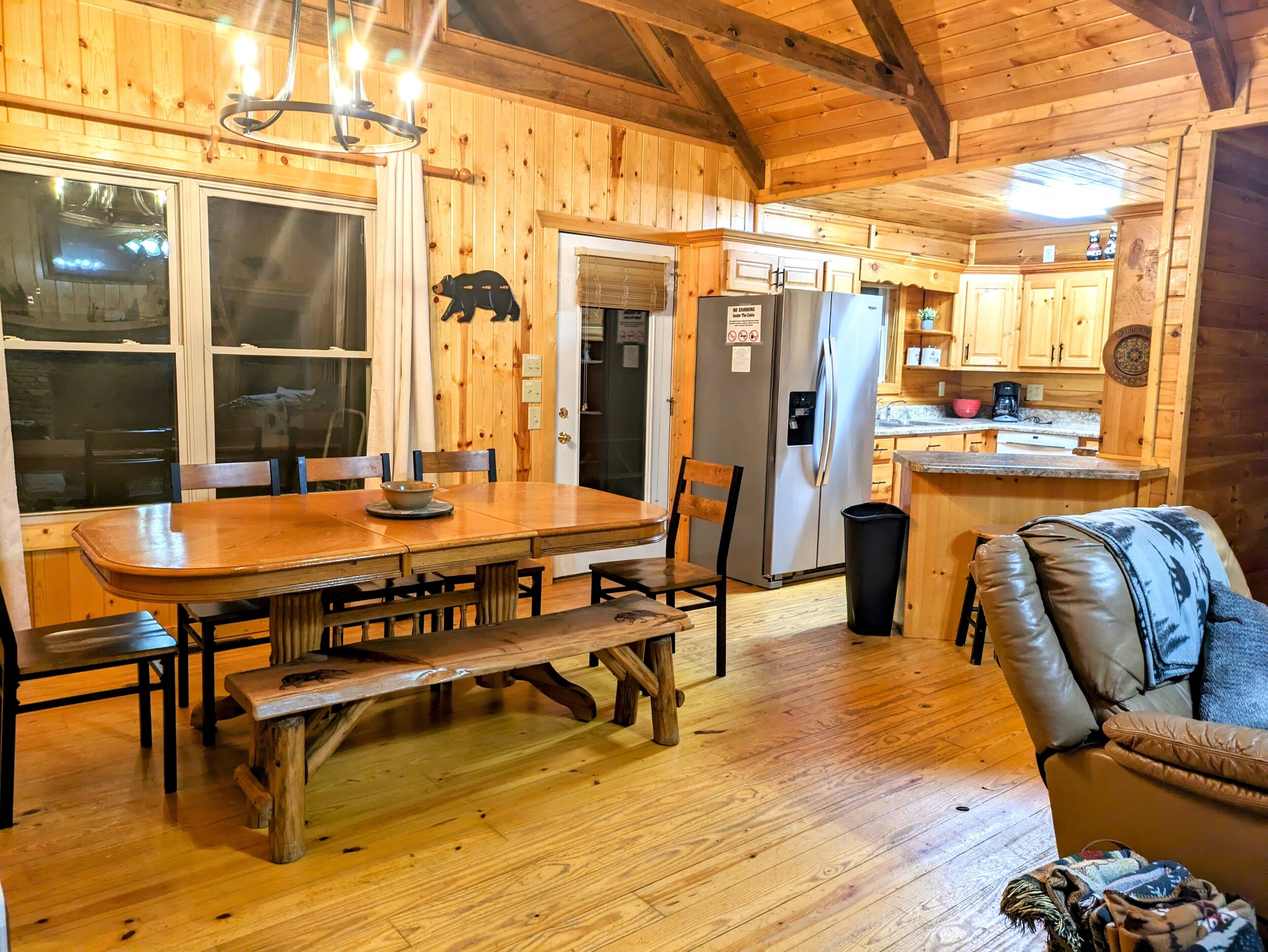 A wooden interior with a dining table, chairs, a bench, a sofa, and a kitchen area with cabinets and a refrigerator.