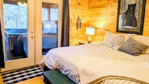A cozy wooden cabin bedroom with a bed, a bench, a nightstand, a lamp, and a framed bear picture on the wall.