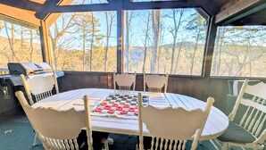 A covered outdoor seating area with a checkered game board, white chairs, and a grill.