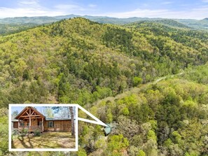 A cabin in a forested area with a view of the surrounding hills.