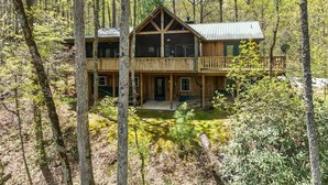 A two-story log cabin with a balcony, surrounded by forest.