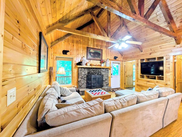 A cozy log cabin interior with a stone fireplace, a large sofa, and a television.