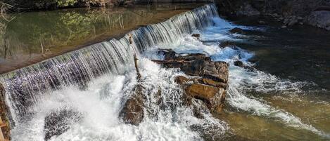 Unes cascades que abracen roques i desemboquen en un riu, envoltades d'arbres.