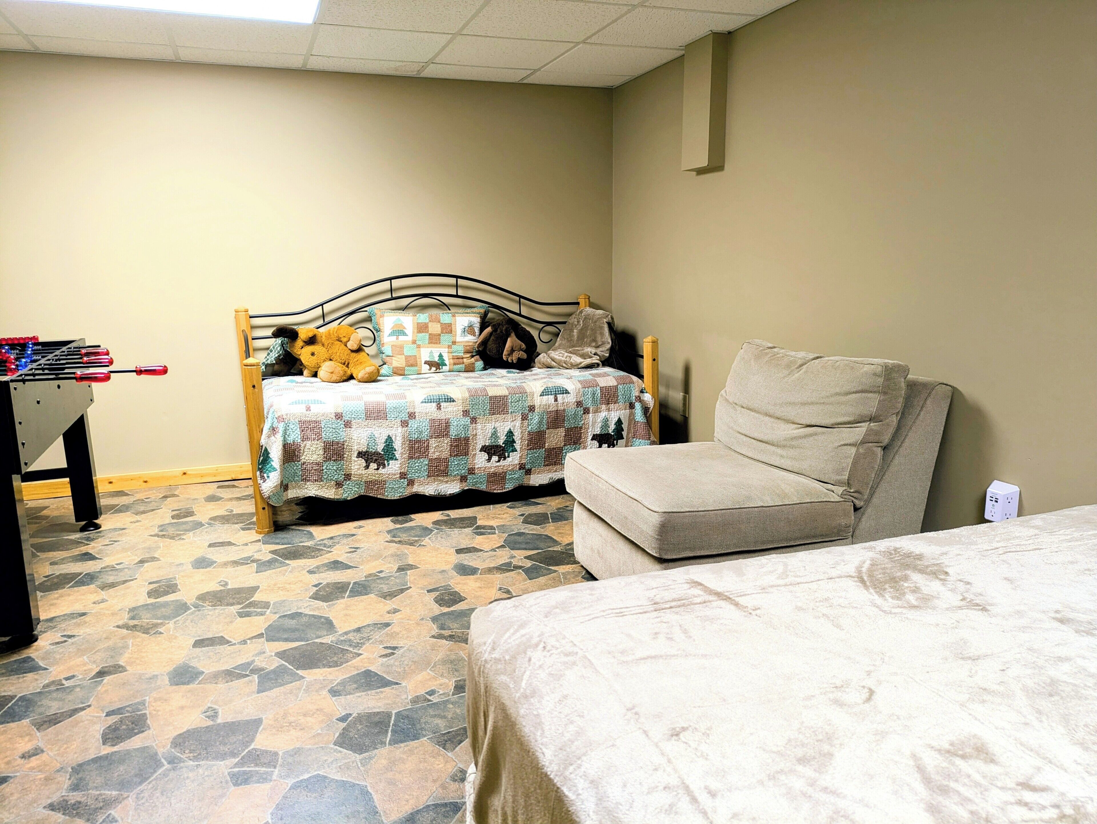 Een slaapkamer met een bed, een bank, een tafelvoetbaltafel en een gewatteerde sprei.