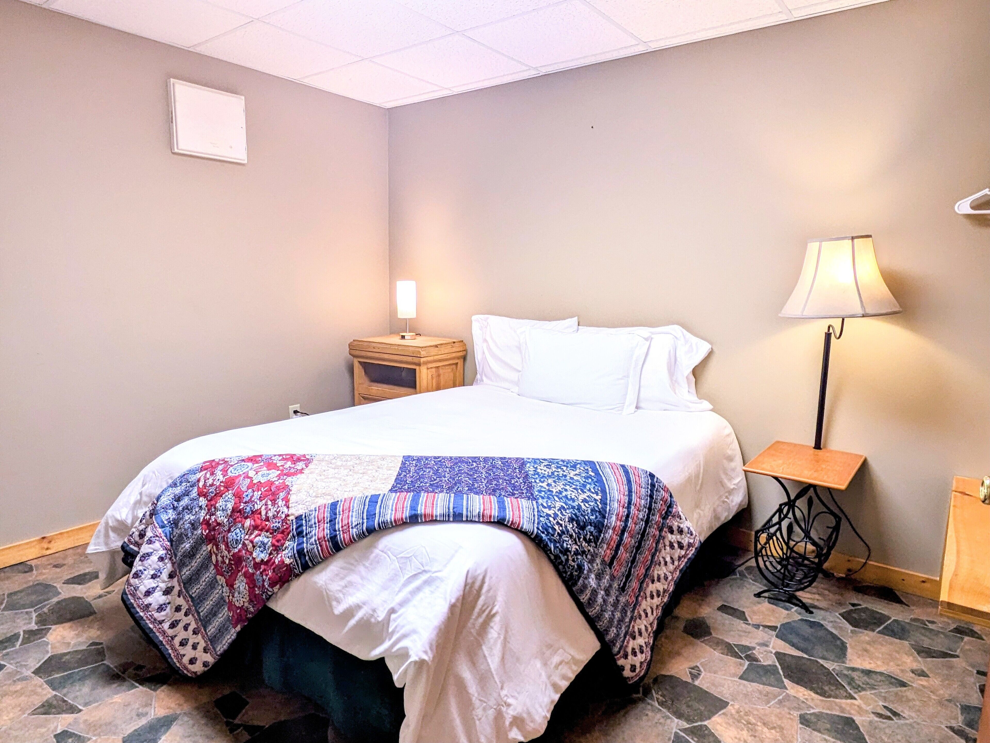 A hotel room with a bed, a nightstand, a lamp, and a wall-mounted light fixture.