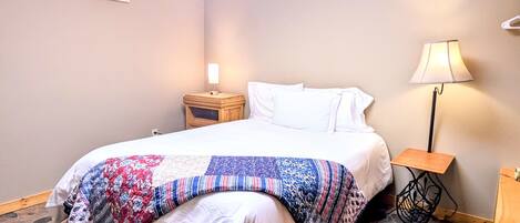 A hotel room with a bed, a nightstand, a lamp, and a wall-mounted light fixture.