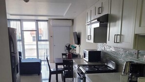 A modern kitchen with white cabinetry, a stainless steel stove, and a microwave. There is a dining area with a table and chairs, and a refrigerator is visible in the corner. -   ROPER'S PLACE...Bayfront apartment/Balcony view Close to Kingston/Airport
 (Portmore)
